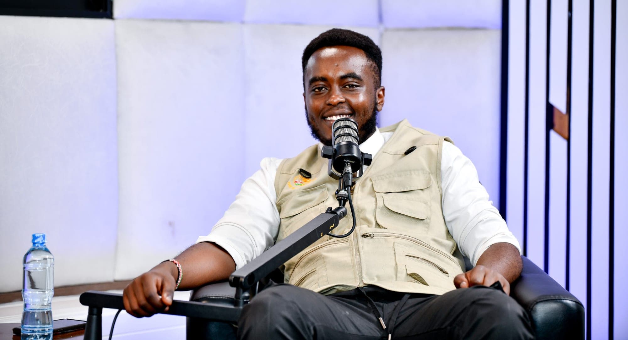 Denzel Maina seated in a podcast studio chair, smiling at the microphone